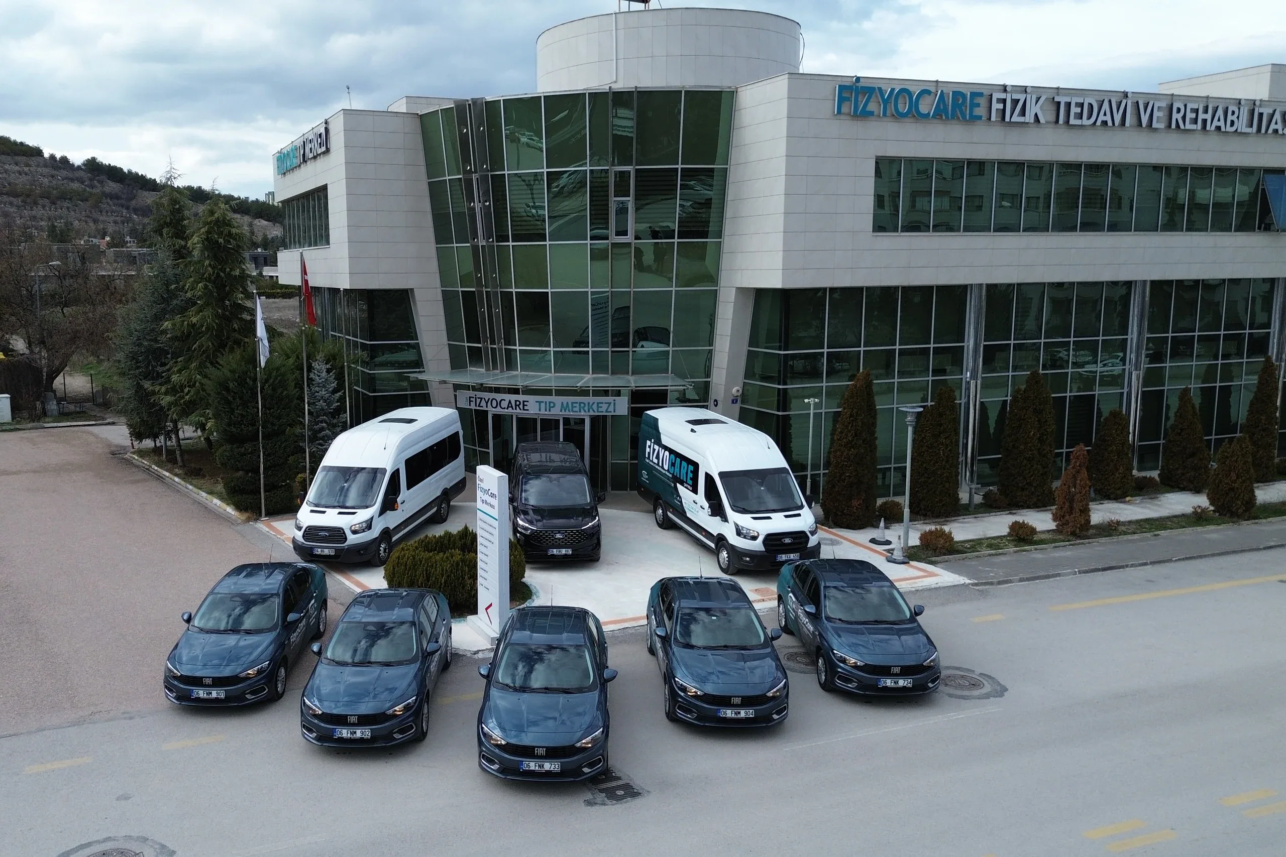 FizyoCare merkez binası önünde sıralanmış hasta servisi minibüsleri ve araç filosu.